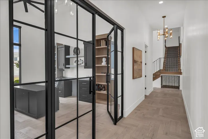 Black-framed glass partition doors, custom built-in shelving, herringbone wood-finish flooring, metal staircase railing, and multi-light chandelier