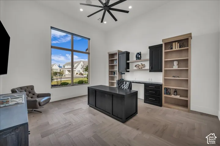 Vaulted ceiling with a large multi-blade ceiling fan, herringbone-pattern wood-finish flooring, floor-to-ceiling windows, and custom built-in cabinetry featuring dark contrast shelving and storage units
