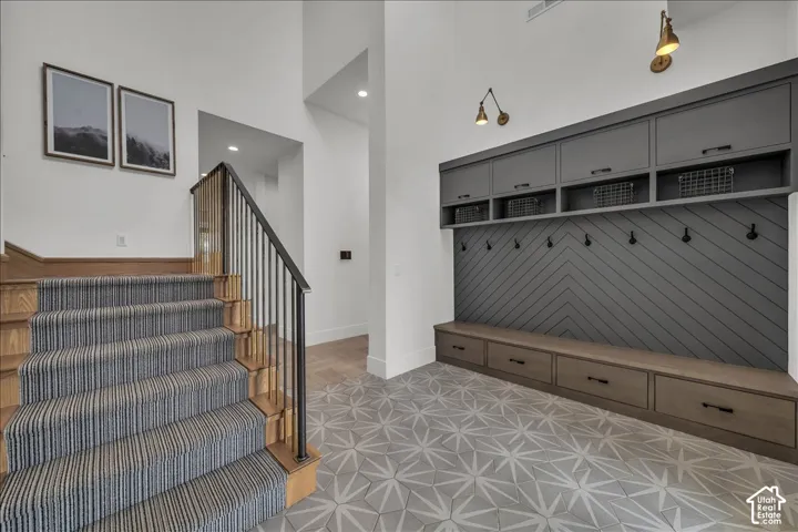Entryway featuring custom floor-to-ceiling built-in cabinetry with integrated bench seating, herringbone-patterned wall paneling, geometric patterned floor tile, and a staircase with metal railing and patterned stair runner