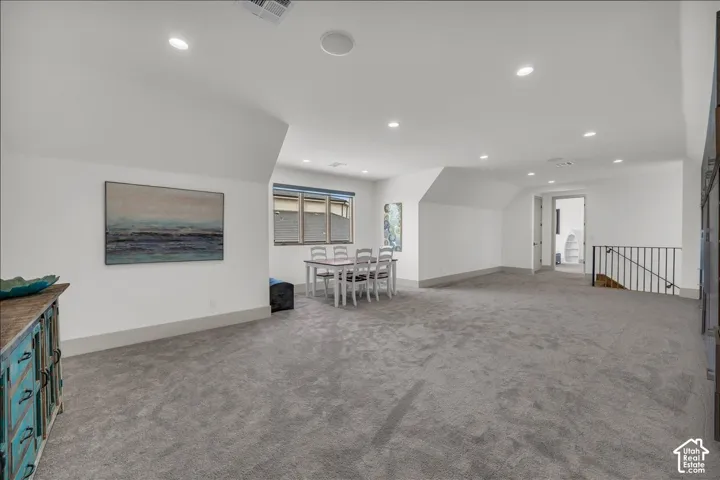 Expansive room featuring recessed lighting, neutral carpeting, vaulted ceilings, and a metal-railing staircase