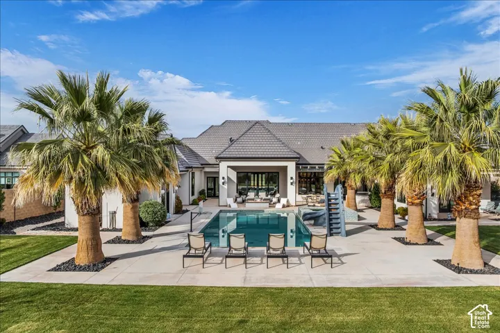 Rear exterior featuring a swimming pool, integrated slide, concrete patio, mature palm trees, and manicured lawn