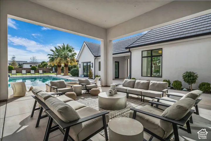 Covered patio featuring concrete tile flooring and recessed lighting, overlooking a swimming pool with stone-surround fire pit and light-colored stucco exterior walls