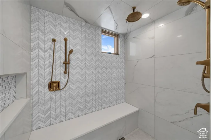 Walk-in shower featuring large-format veined tile, chevron-patterned tile wall accents, a built-in bench, metallic hardware, and a recessed wall niche