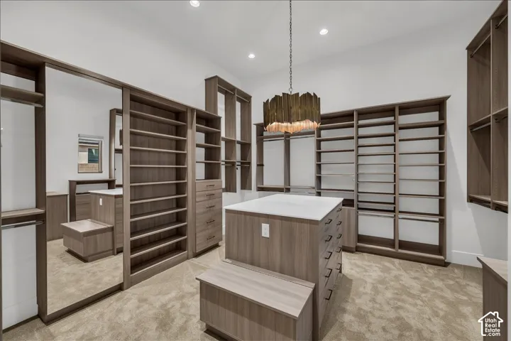 Custom wood-finish cabinetry featuring extensive shelving, a central island with a solid surface countertop, integrated full-length mirror, recessed lighting, and a metallic chandelier