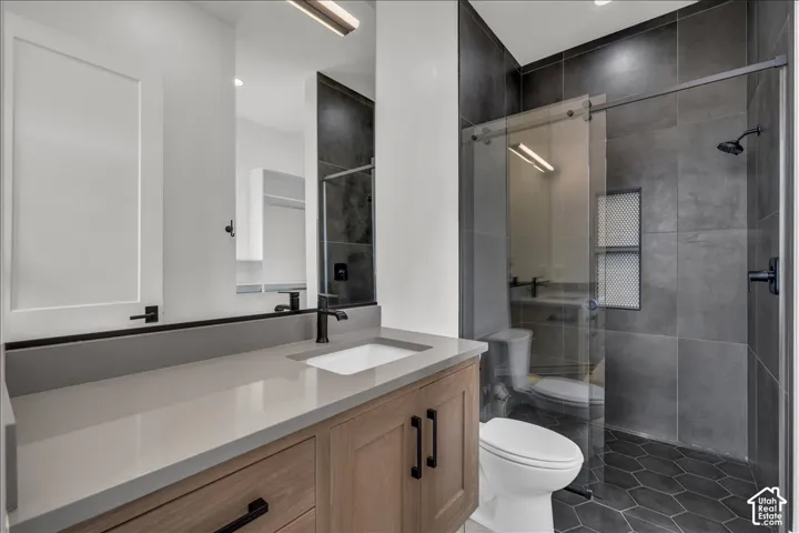 Bathroom featuring wood-finish cabinetry, a rectangular undermount sink, quartz countertop, matte black hardware, and a walk-in shower with large-format wall tiles and hexagonal floor tiles