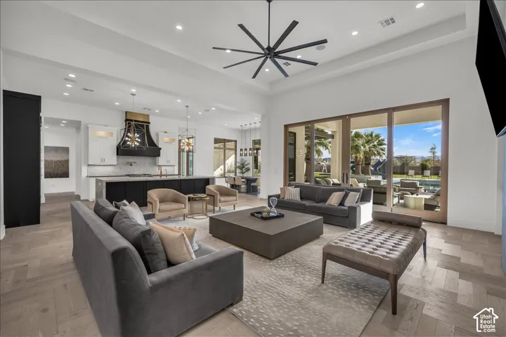 Open-concept area featuring herringbone wood-finish flooring, high tray ceilings, a modern multi-blade ceiling fan, and expansive sliding glass doors