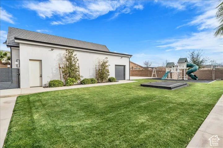 Expansive backyard featuring a manicured lawn, concrete patio, perimeter masonry wall, and low-maintenance landscaping