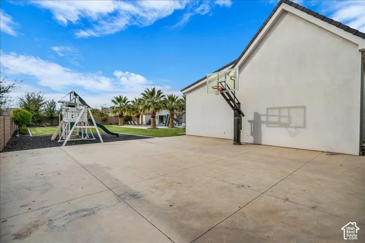 Backyard featuring a concrete sport court, wall-mounted basketball hoop, turf surfacing, and mature palm trees