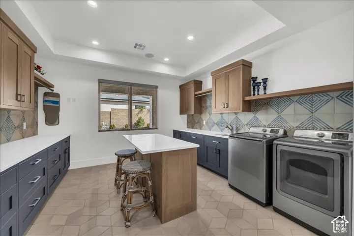 Laundry room featuring two-tone cabinetry, quartz countertops, a center island, geometric patterned tile backsplash, and hexagonal floor tile