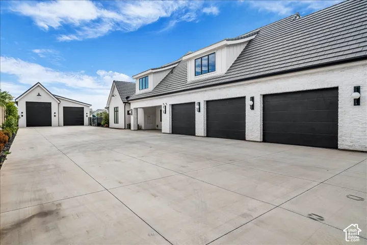 White brick exterior featuring dark-toned multi-car garage doors, concrete driveway, and gabled roofline with dormer windows
