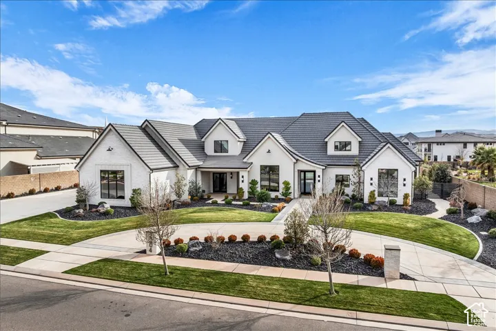 Custom white-painted brick exterior featuring a multi-gabled roofline, dark-toned tile roofing, a circular concrete driveway, and landscaped grounds with decorative stone mulch and manicured turf