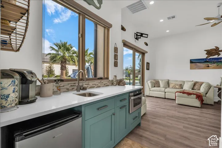 Wet bar featuring solid-surface countertops, teal cabinetry, under-counter refrigeration, built-in microwave, and tile backsplash