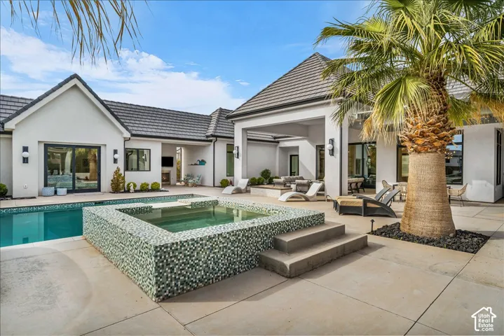 Backyard oasis featuring a concrete patio, integrated tiled spa, swimming pool, covered outdoor living area, and mature palm tree