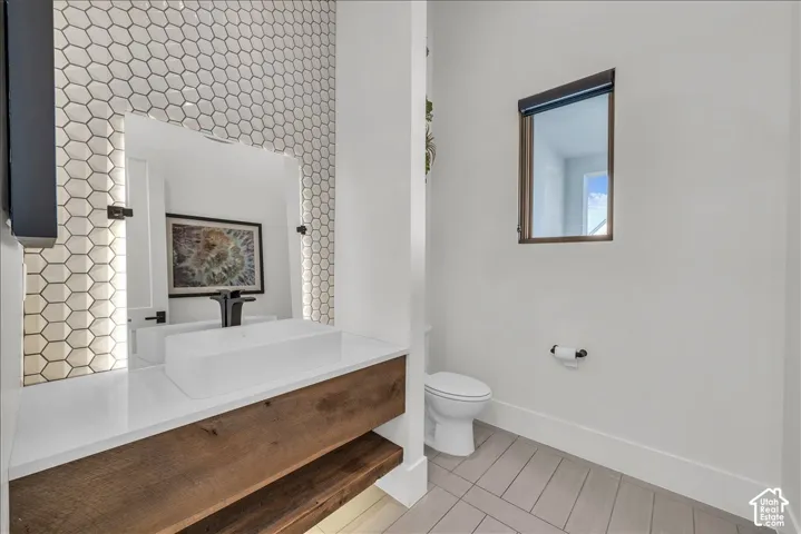 Floating vanity with wood-finish cabinetry, white countertop, rectangular vessel sink, wall-mounted matte black faucet, and hexagon-tiled accent wall