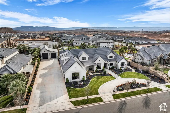 Modern white exterior featuring a steep-pitched tile roof, multi-car garage, circular concrete driveway, and manicured landscaping