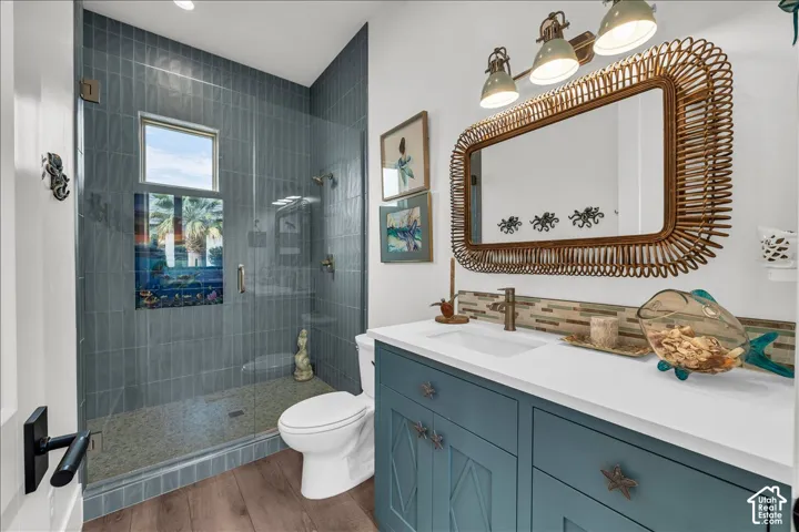 Bathroom featuring a blue-toned vanity with a white countertop, walk-in shower with floor-to-ceiling tile, pebble-texture shower floor, and wood-finish flooring