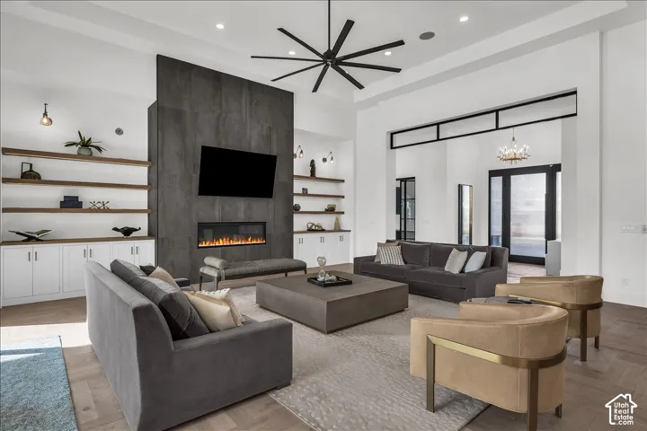 High ceiling with recessed lighting and a large ceiling fan, floor-to-ceiling stone-surround fireplace, custom built-in shelving, wood-finish flooring, and architectural transom window detailing