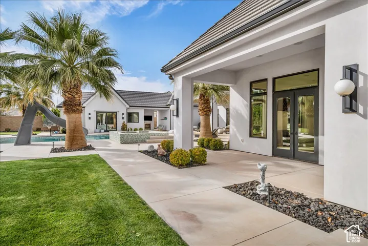 Covered patio featuring concrete hardscaping, manicured lawn, pool with built-in slide, and exterior wall-mounted globe lighting
