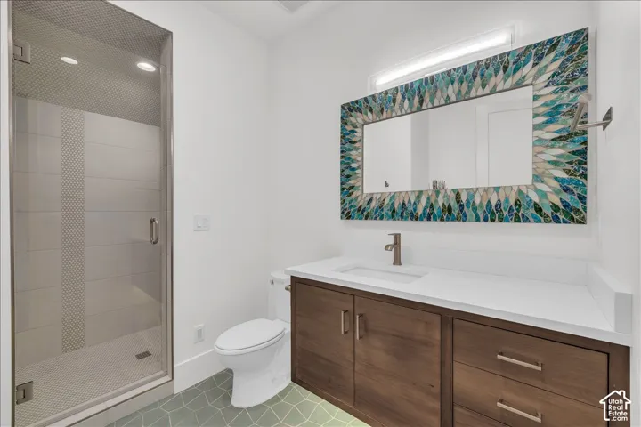 Bathroom featuring a walk-in shower with glass enclosure, custom mosaic-tiled mirror, wood-finish vanity with white countertop, and geometric floor tiling