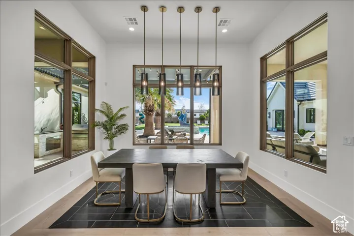 Dining area featuring floor-to-ceiling windows, five geometric pendant lights, and a decorative tile inlay surrounded by light-toned wood-finish flooring