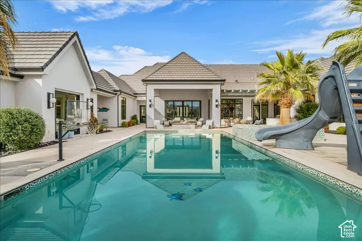 Rectangular swimming pool featuring a built-in water slide, tile surround, covered patio area, and concrete decking
