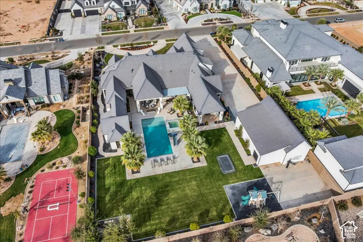 Aerial perspective of a property featuring a swimming pool, integrated spa, covered patio, manicured lawn, and hardscaped sport court