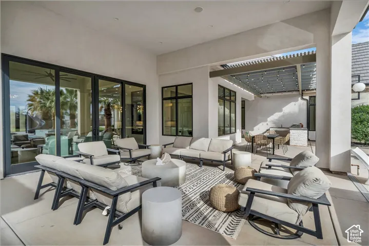 Covered patio featuring concrete flooring, multi-panel sliding glass doors, a stone-accented outdoor kitchen, and a wooden pergola structure