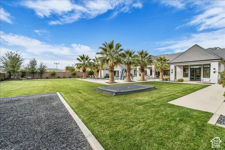 Expansive backyard featuring a large grass lawn, perimeter masonry wall, swimming pool with in-ground slide, and mature palm trees