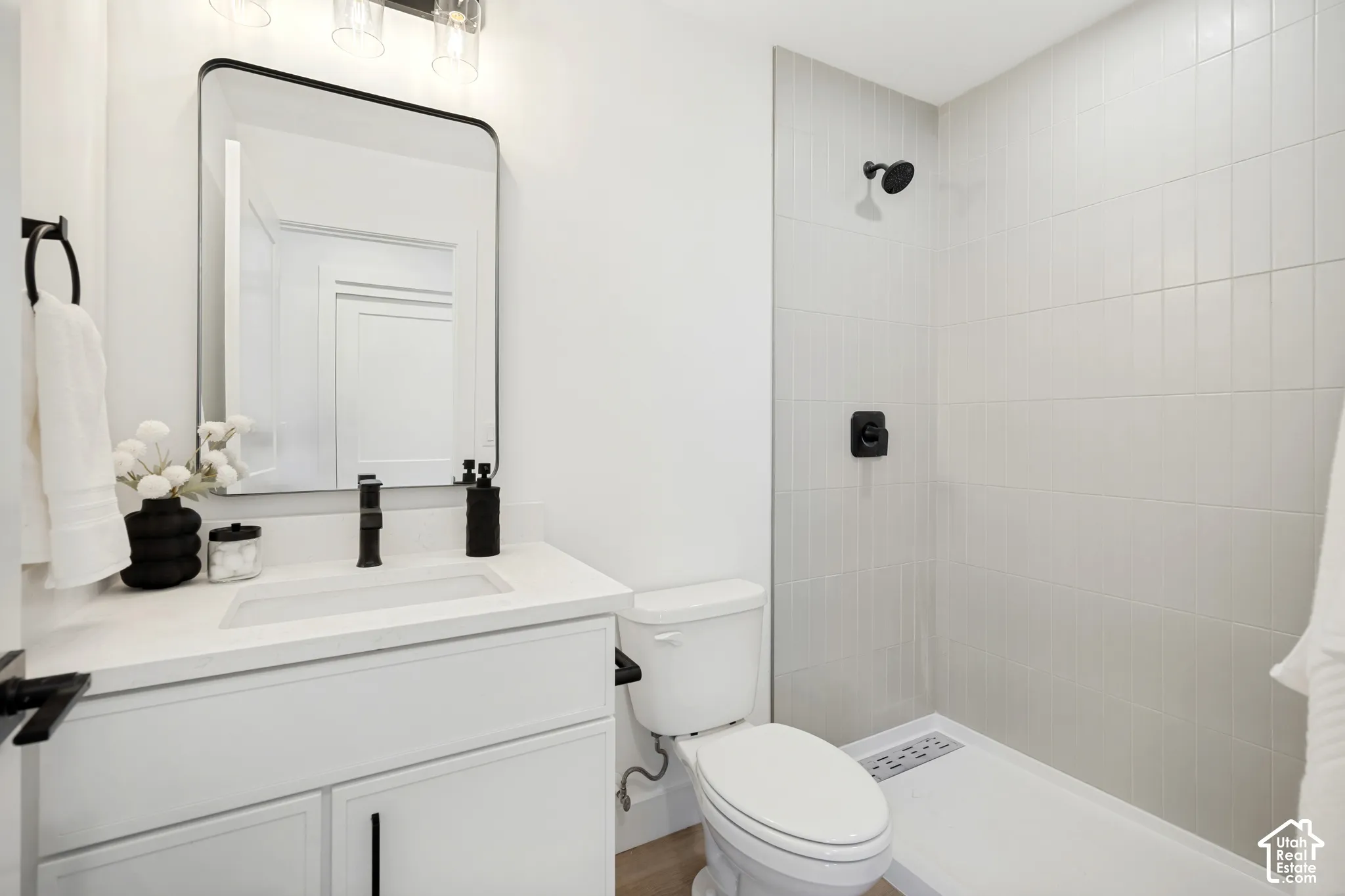 White vanity with a solid surface countertop, rectangular undermount sink, matte black faucet, rectangular mirror with a black frame, and a walk-in shower with vertical wall tile and matte black fixtures