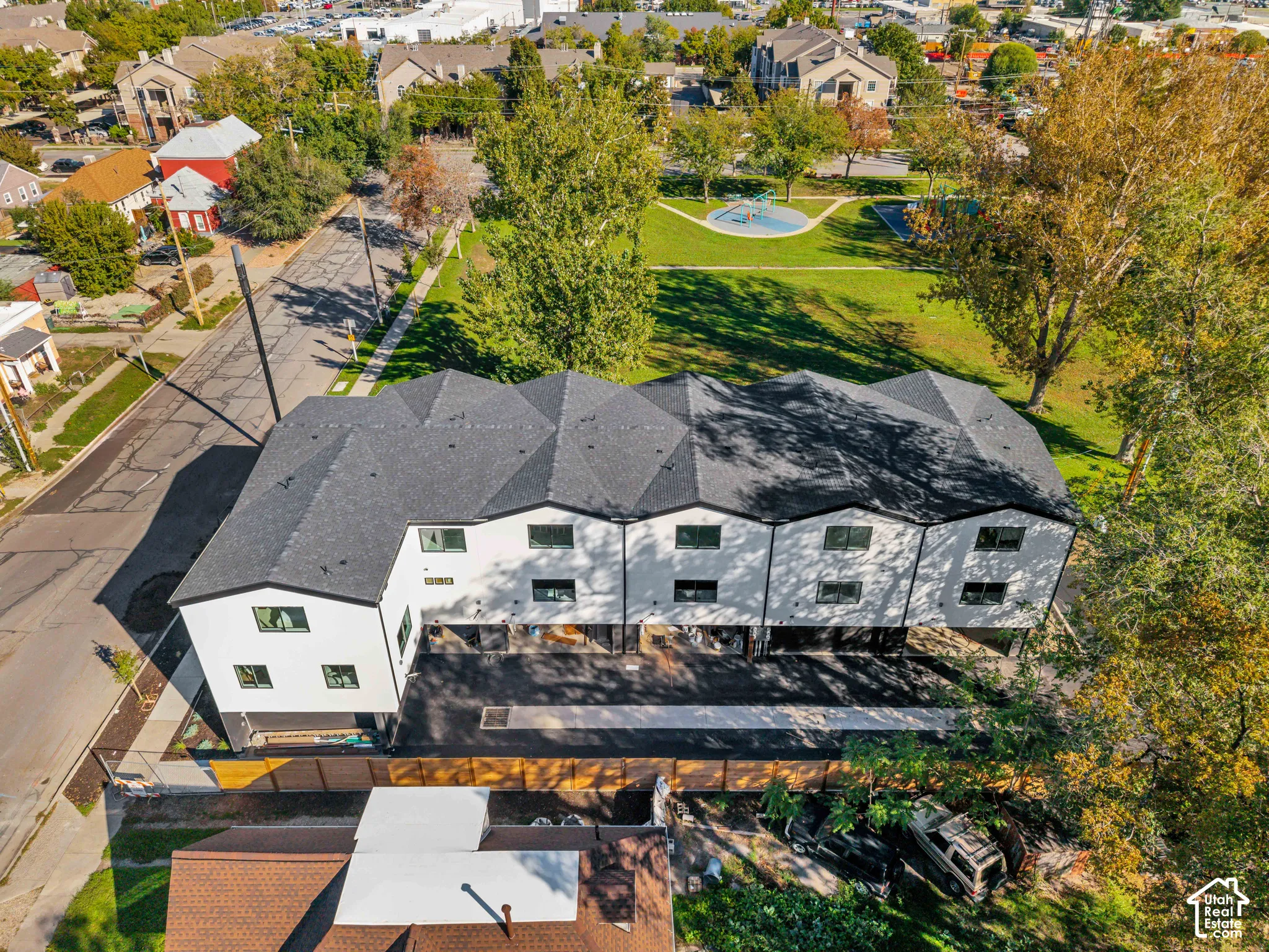 Multi-unit residential property featuring a dark asphalt shingle roof, white exterior siding, attached ground-level garages, and paved driveway access