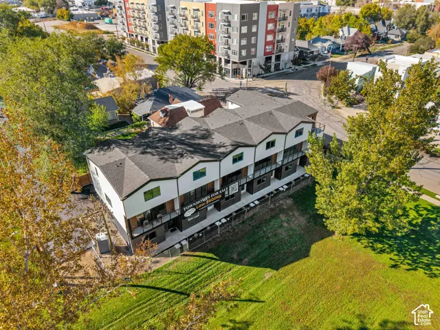Multi-unit residential structure featuring a dark shingle roof, white and dark-toned siding, private balconies, and hardscaped driveway