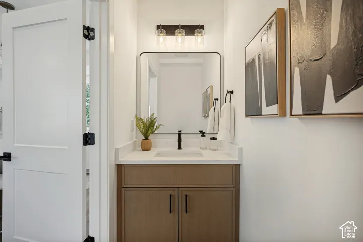 Vanity featuring wood-finish cabinetry, a rectangular undermount sink, a stone-surface countertop, a matte black faucet, and a rectangular mirror with a metal frame
