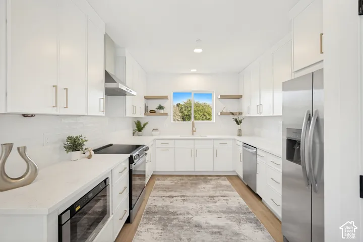 Kitchen featuring white shaker-style cabinetry, quartz countertops, stainless steel appliances, open wood-finish shelving, and wood-finish flooring
