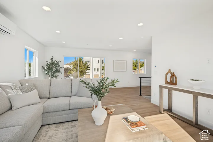 Open-concept space featuring wood-finish flooring, recessed lighting, wall-mounted climate control unit, and white walls
