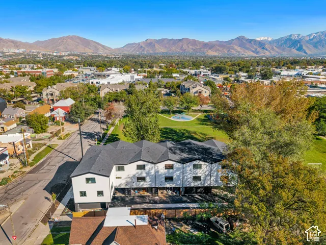 Multi-level residence featuring a white exterior, dark-toned roof, integrated garage bays, and proximity to expansive green space with mountain backdrops