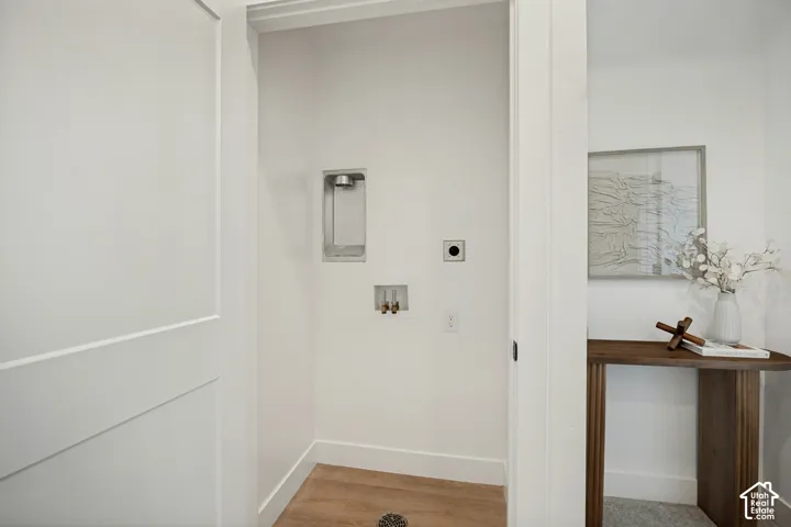 Utility area featuring wood-finish flooring, recessed plumbing connections, and a dedicated floor drain