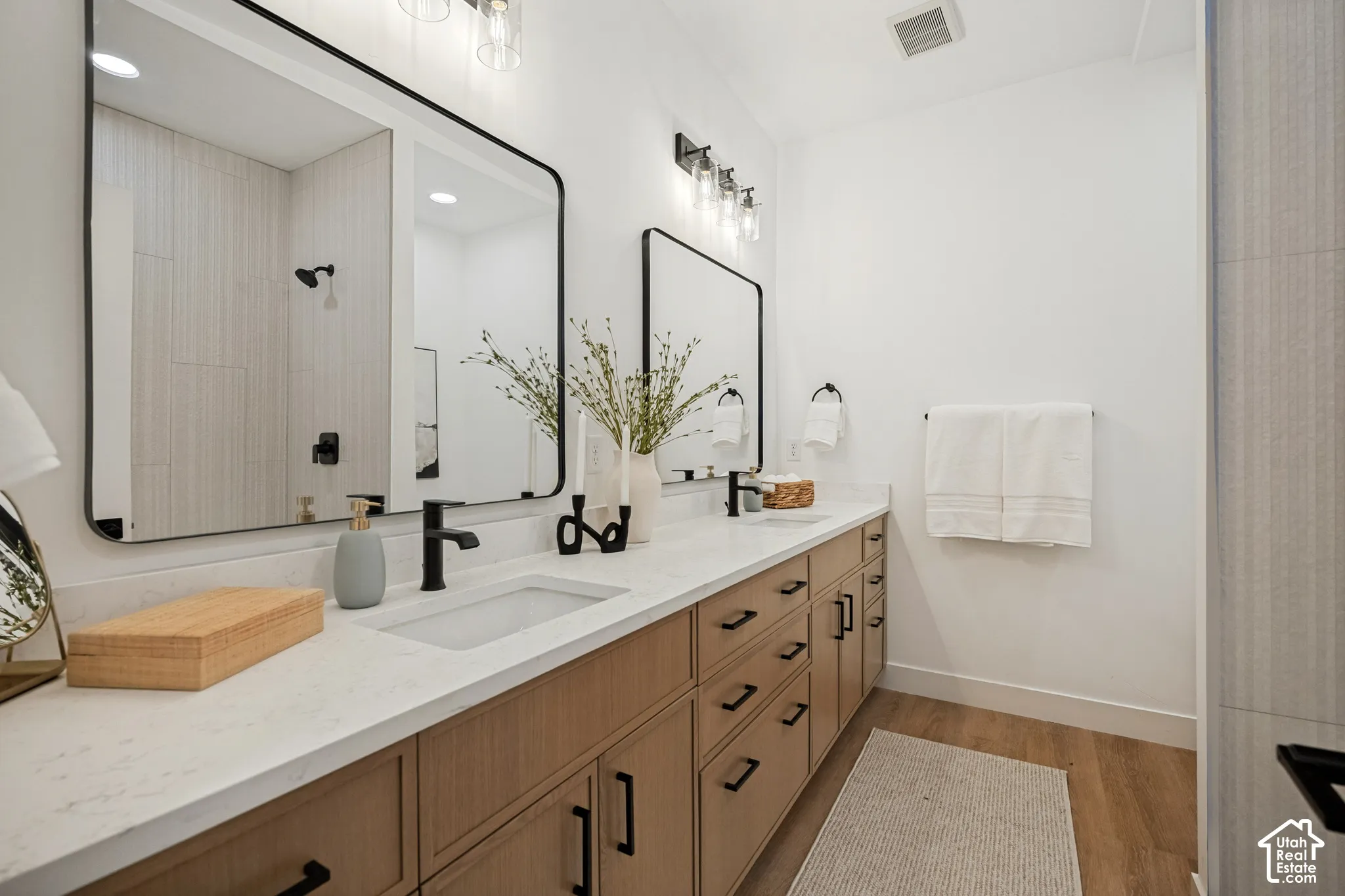 Dual vanity featuring light-toned cabinetry, quartz countertops, integrated rectangular sinks, matte black hardware, and large mirrors with rounded corners