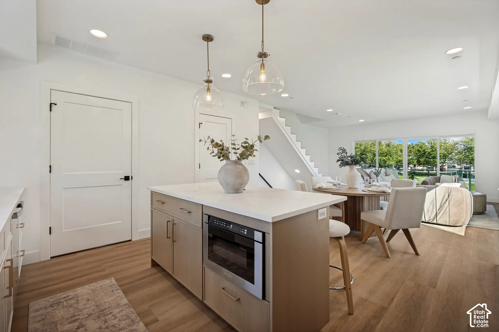 Kitchen island featuring a stone-composite countertop, light wood cabinetry, and a built-in stainless steel microwave, complemented by dual glass globe pendant lights and wide-plank wood-finish flooring