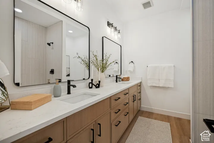Dual vanity featuring light-toned cabinetry, quartz countertops, integrated rectangular sinks, matte black hardware, and large mirrors with rounded corners