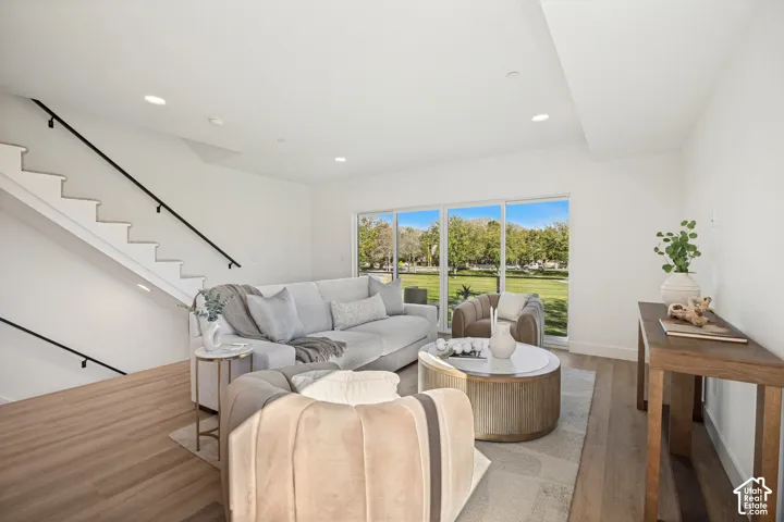 Open-concept room featuring wood-finish flooring, recessed lighting, and a staircase with a black metal handrail, complemented by large sliding glass doors
