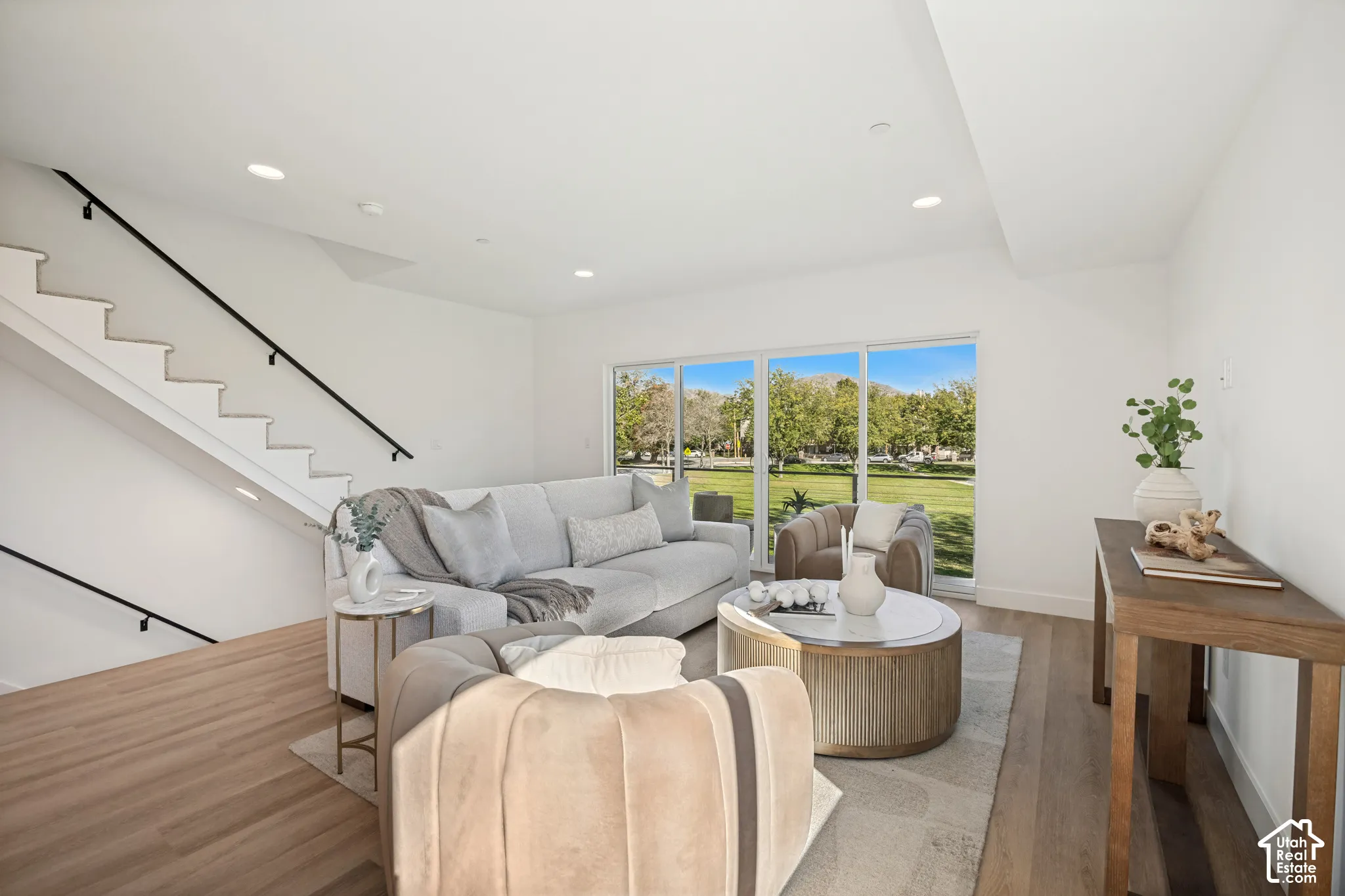 Open floor plan featuring wood-finish flooring, recessed lighting, large sliding glass doors, and a staircase with a black metal handrail