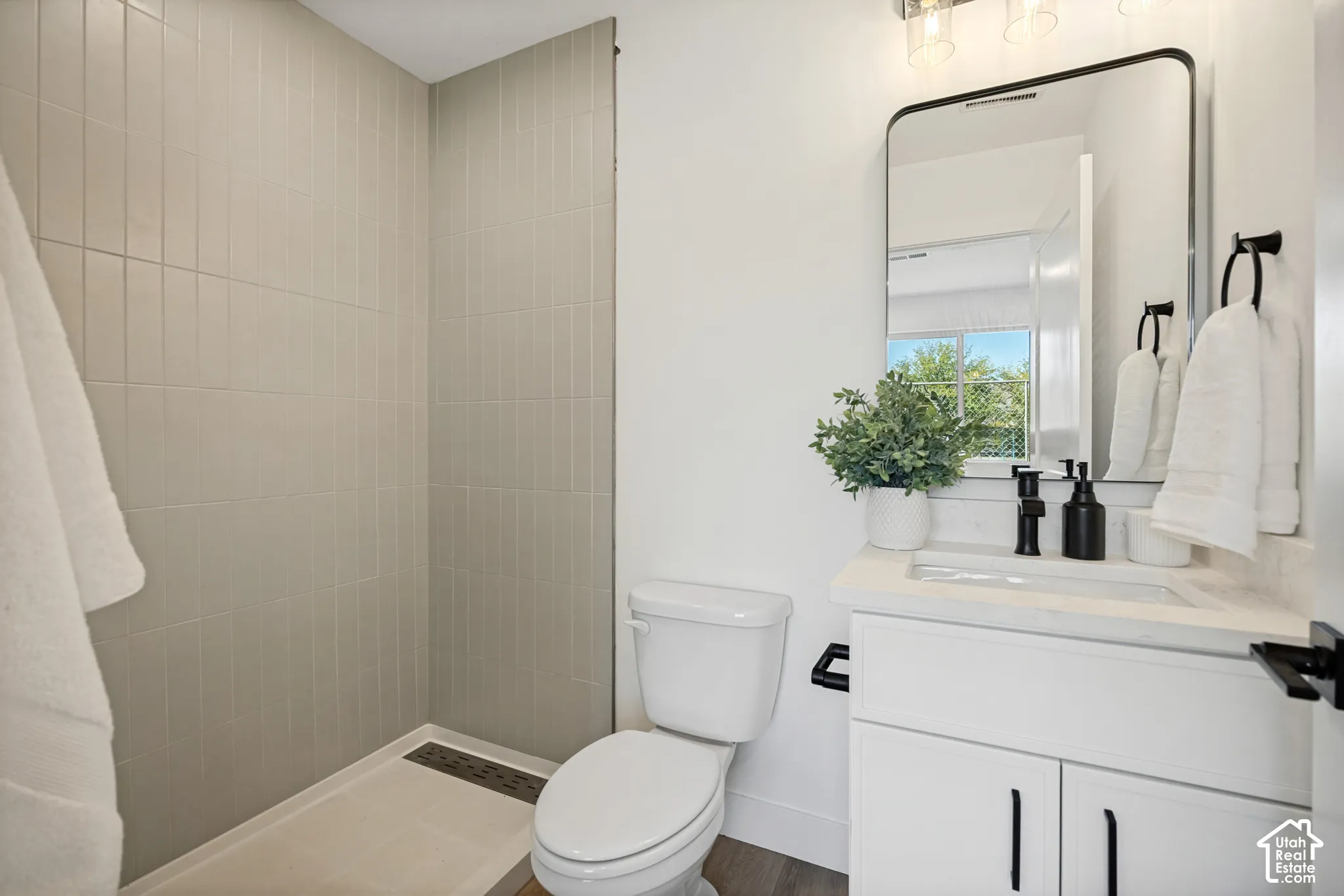 Bathroom featuring a glass-enclosed shower with vertical wall tile, white vanity with stone-composite countertop, matte black faucet and hardware, and a rounded-edge vanity mirror