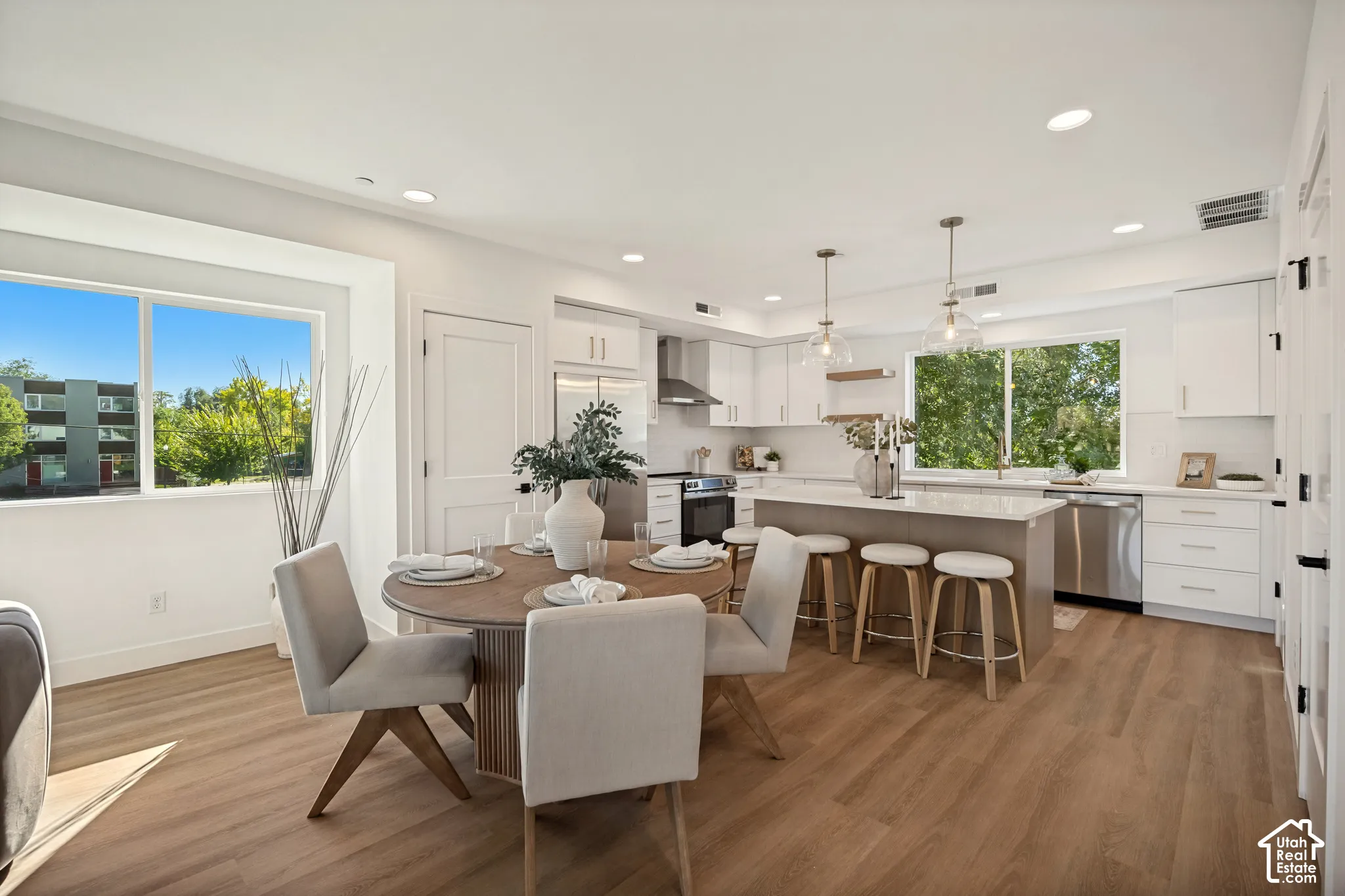 Kitchen featuring white shaker-style cabinetry, a central island with quartz countertops, stainless steel appliances, pendant lighting, and wood-finish flooring
