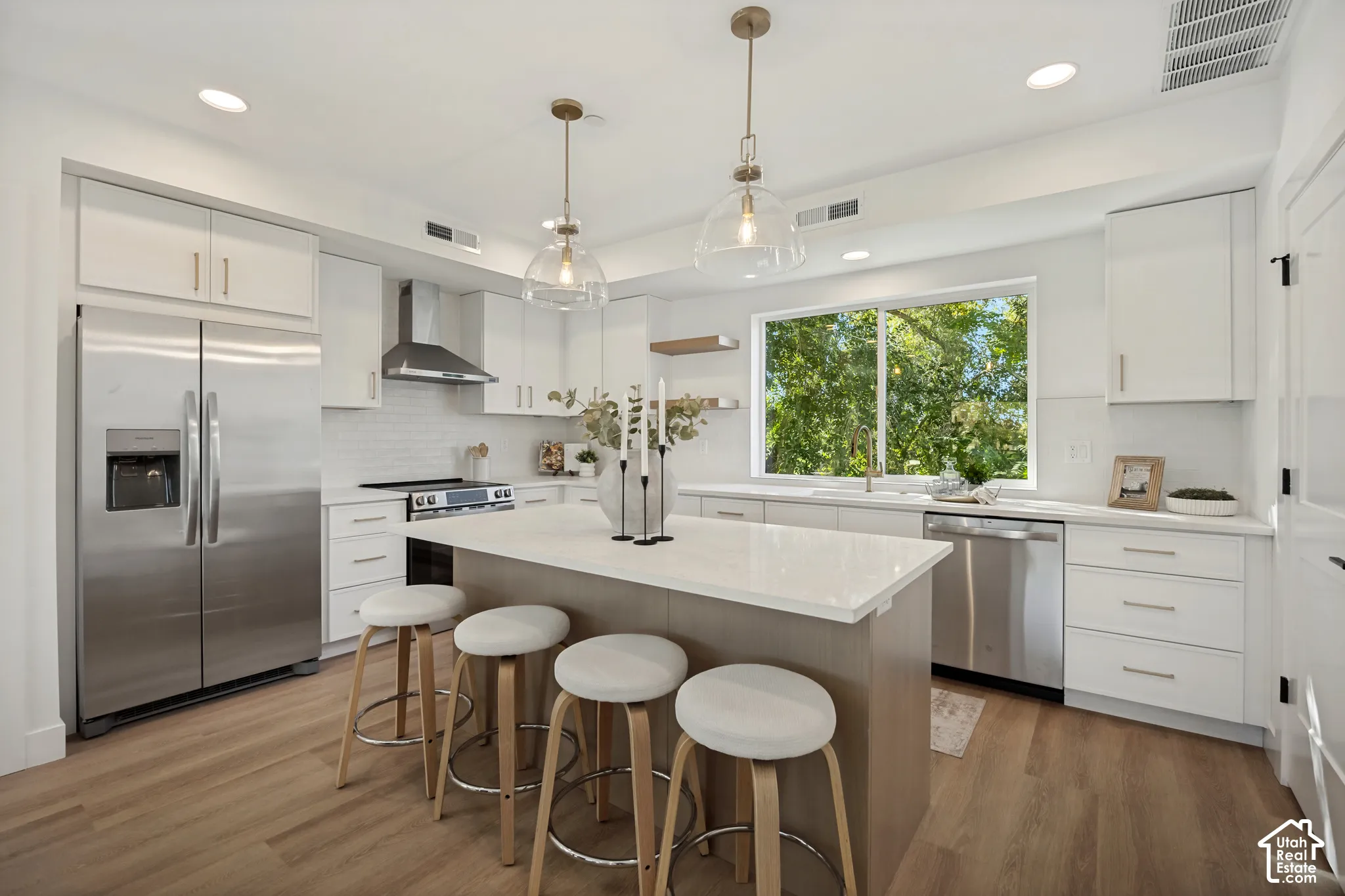 Kitchen featuring a center island with a stone countertop, white cabinetry, stainless steel appliances, pendant lighting, and wood-finish flooring