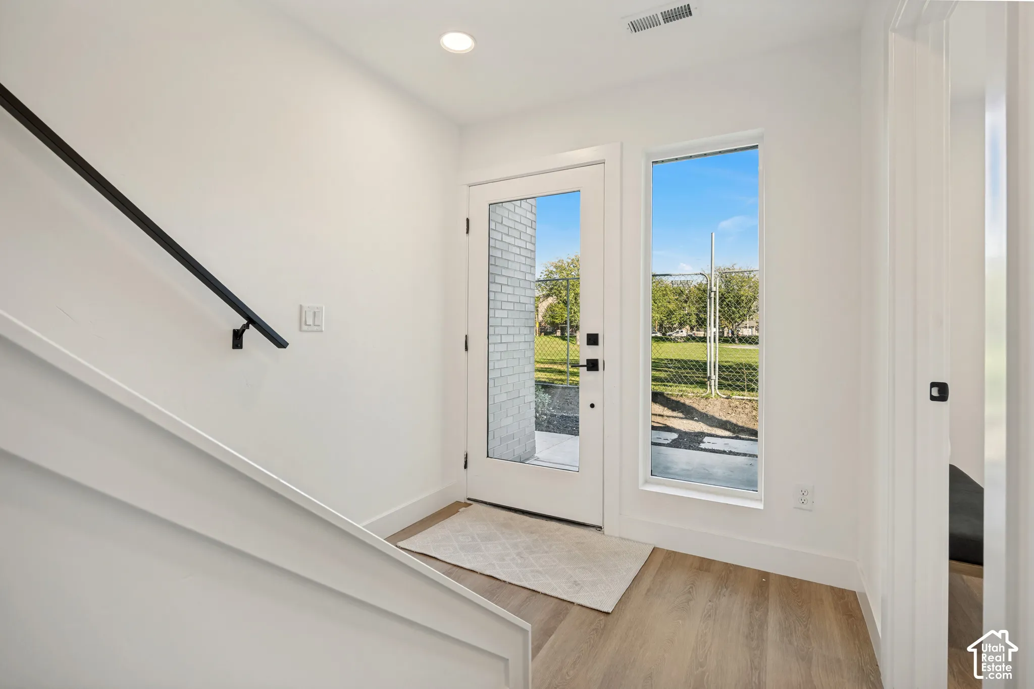 Entryway featuring wood-finish flooring, a glass-panel exterior door, a full-length side window, and a matte black metal handrail