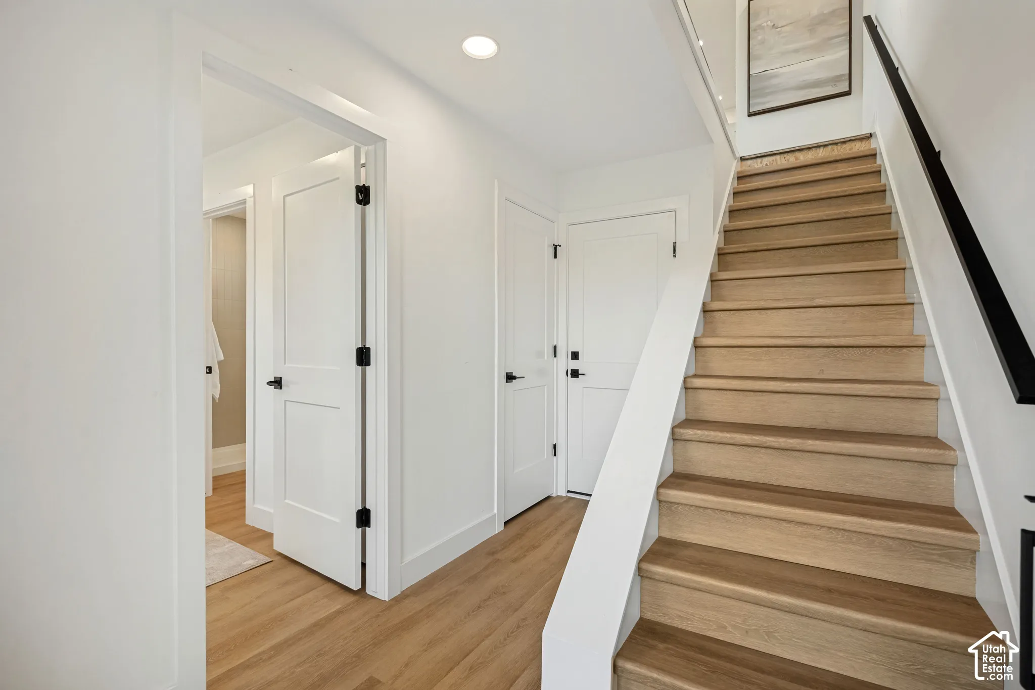 Staircase featuring wood-finish treads, white risers, and a matte black handrail