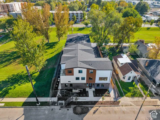 Multi-level building featuring a modern mix of white stucco, dark brick, and vertical wood-finish siding, accented by an asphalt shingle roof and a concrete walkway