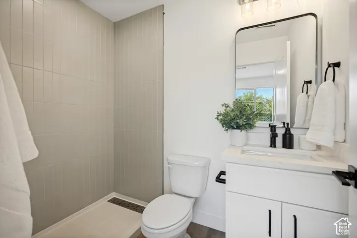 Bathroom featuring a glass-enclosed shower with vertical wall tile, white vanity with stone-composite countertop, matte black faucet and hardware, and a rounded-edge vanity mirror
