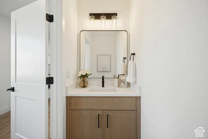 Wood-finish vanity cabinet with a stone countertop, rectangular undermount sink, matte black faucet, rounded-corner mirror, and three-light wall fixture