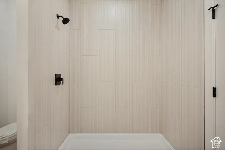 Shower enclosure featuring vertical light-toned textured tile, matte black wall-mounted showerhead, and matching single-handle pressure balance valve